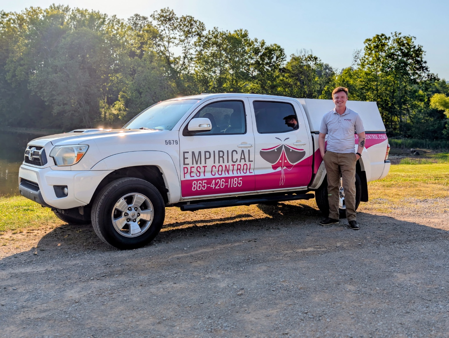 Bay Cravens standing next to the Empirical Pest Control truck by a lake in Rockwood, TN